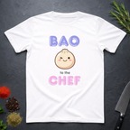 White t-shirt with cartoon bun and text 'BAO to the CHEF' on a dark surface with kitchen items.
