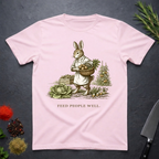Light pink t-shirt with a rabbit illustration and 'Feed People Well' text on a dark surface.