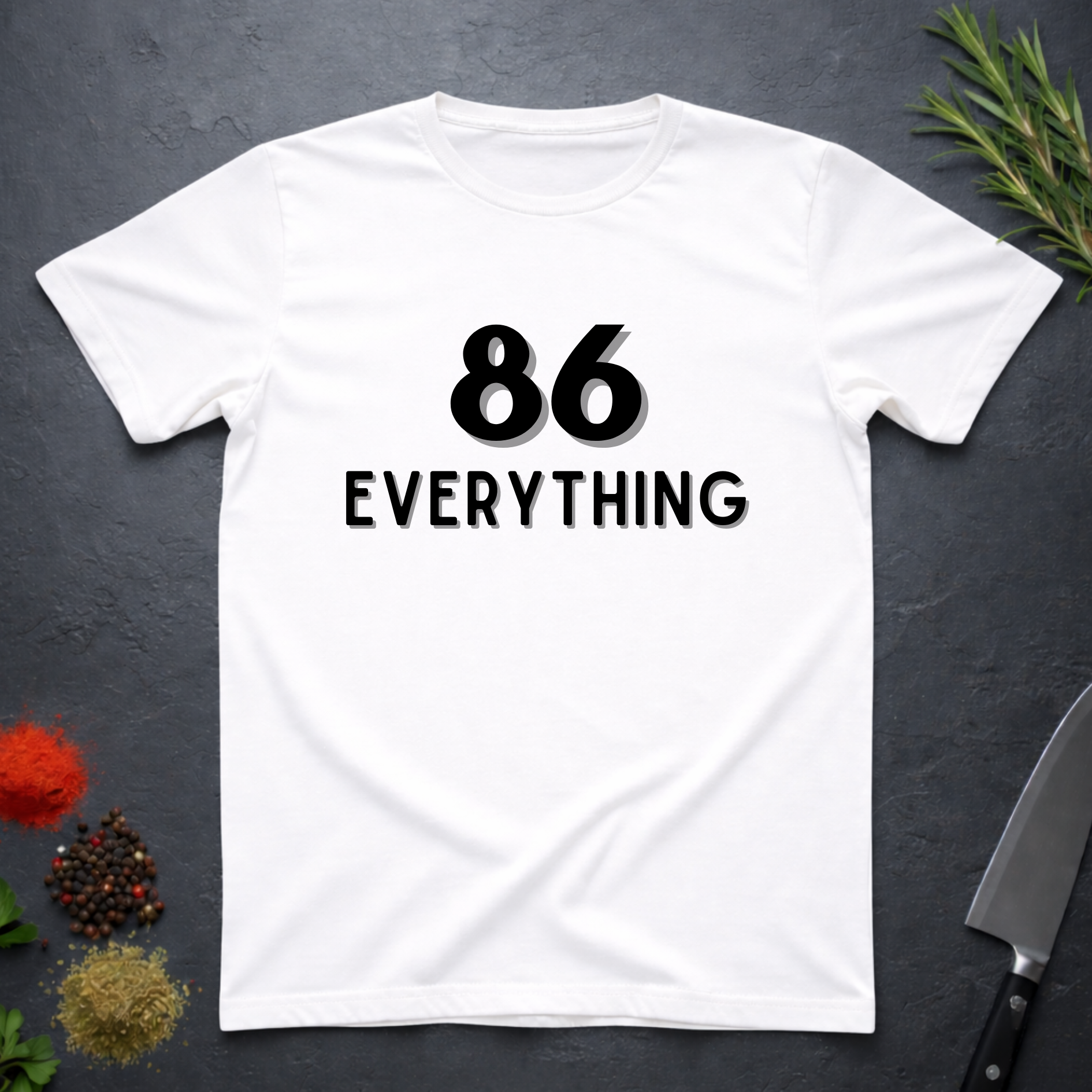 White t-shirt with '86 EVERYTHING' text on a dark surface with decorative elements.