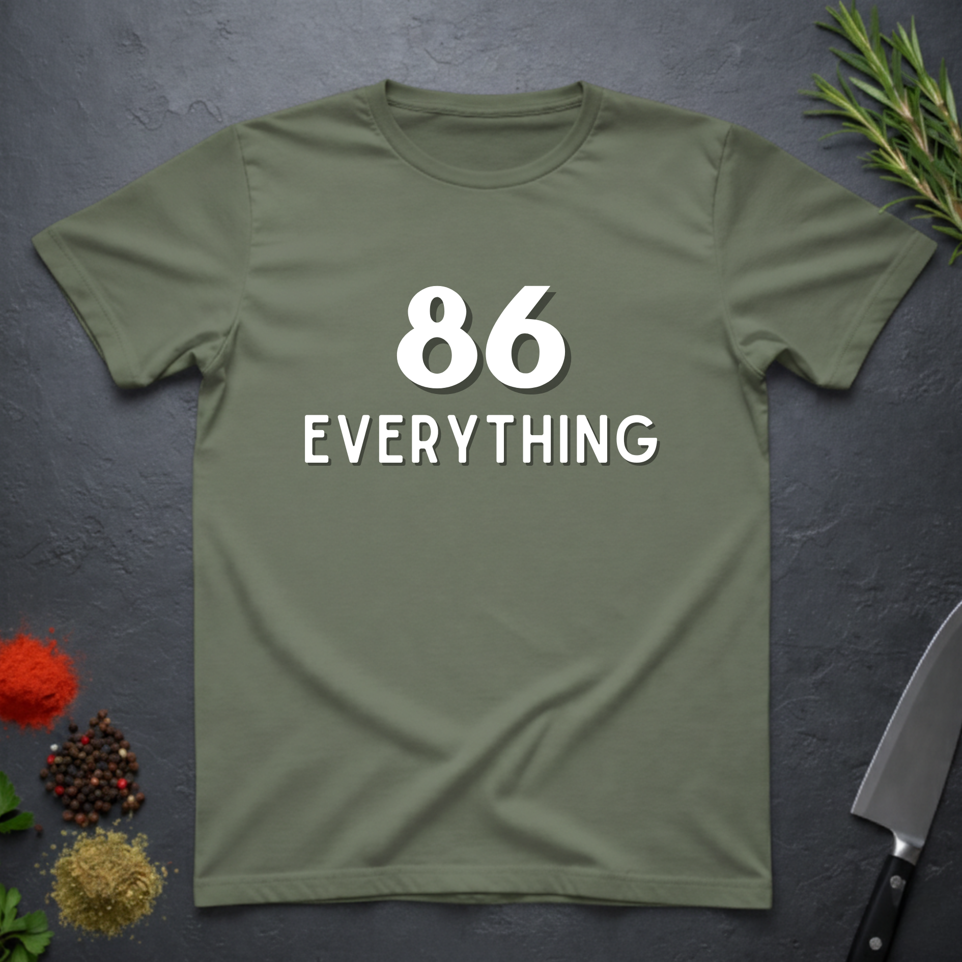 Military Green t-shirt with '86 EVERYTHING' text on a dark surface with kitchen items.