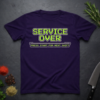 Purple t-shirt with green text "Service Over-Press Start for Next Shift" on a dark surface.