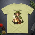 Pistachio green t-shirt with a anime type elf character cooking over a fire, text 'Cook with Magic', on a dark surface with kitchen items.