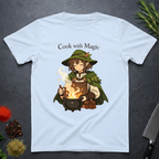 Light Blue t-shirt with a anime type elf character cooking over a fire, text 'Cook with Magic', on a dark surface with kitchen items.