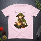 Light Pink t-shirt with a anime type elf character cooking over a fire, text 'Cook with Magic', on a dark surface with kitchen items.
