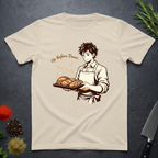 Sand colored t-shirt with a graphic of a baker holding bread and text 'Up Before Dawn' on a dark surface.