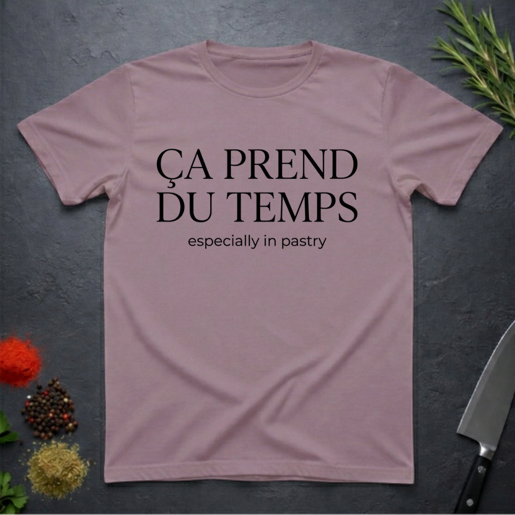 Paragon colored t-shirt with text 'ÇA PREND DU TEMPS especially in pastry' on a dark surface with kitchen items.