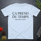 Light Blue t-shirt with text 'Ca prend du temps especially in pastry' on a dark surface with kitchen items.
