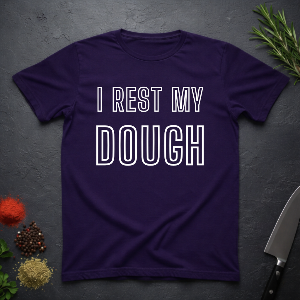 Purple t-shirt with 'I Rest My Dough' text on a dark surface with kitchen items.