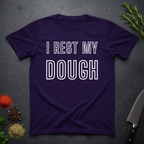 Purple t-shirt with 'I Rest My Dough' text on a dark surface with kitchen items.