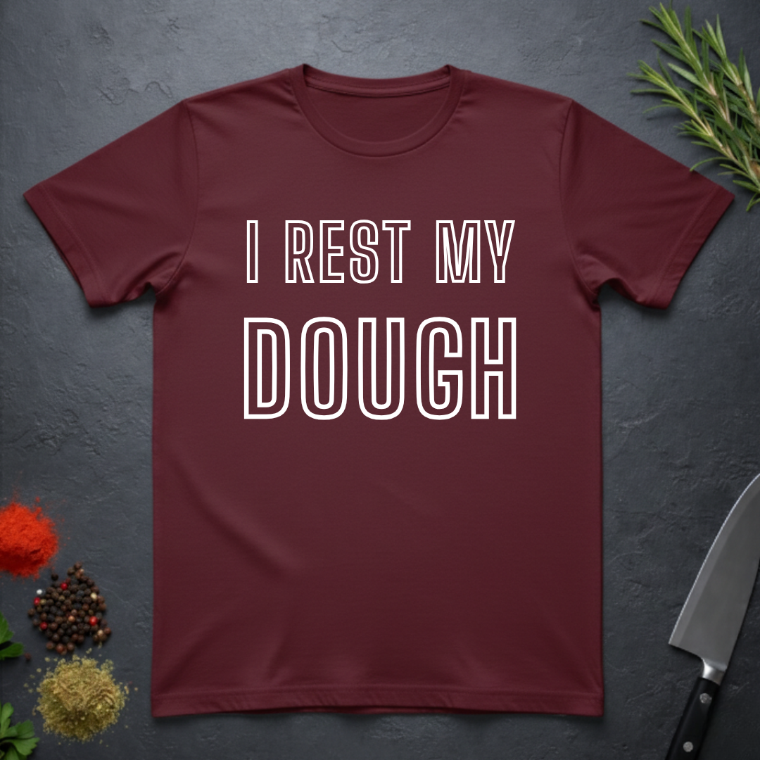 Maroon t-shirt with 'I REST MY DOUGH' text on a dark surface with decorative elements.
