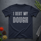 Navy blue t-shirt with 'I REST MY DOUGH' text on a dark surface with kitchen items.