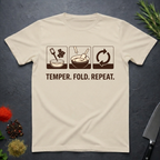 Sand colored t-shirt with chocolate-making diagram and text 'Temper. Fold. Repeat.' on a dark surface.