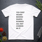 White t-shirt with list of back of house kitchen words in black text on a dark surface with kitchen items.