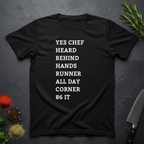 Black t-shirt with list of back of house kitchen words in white text on a dark surface with kitchen items.