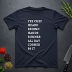 Navy blue t-shirt with list of back of house kitchen words in white text on a dark surface with kitchen items.