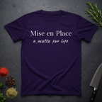 Amethyst Purple t-shirt with 'Mise en Place a motto for life' text on a dark surface with kitchen items.
