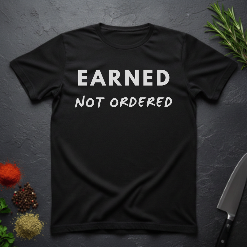 Black t-shirt with 'Earned Not Ordered' text on a dark surface with decorative elements.