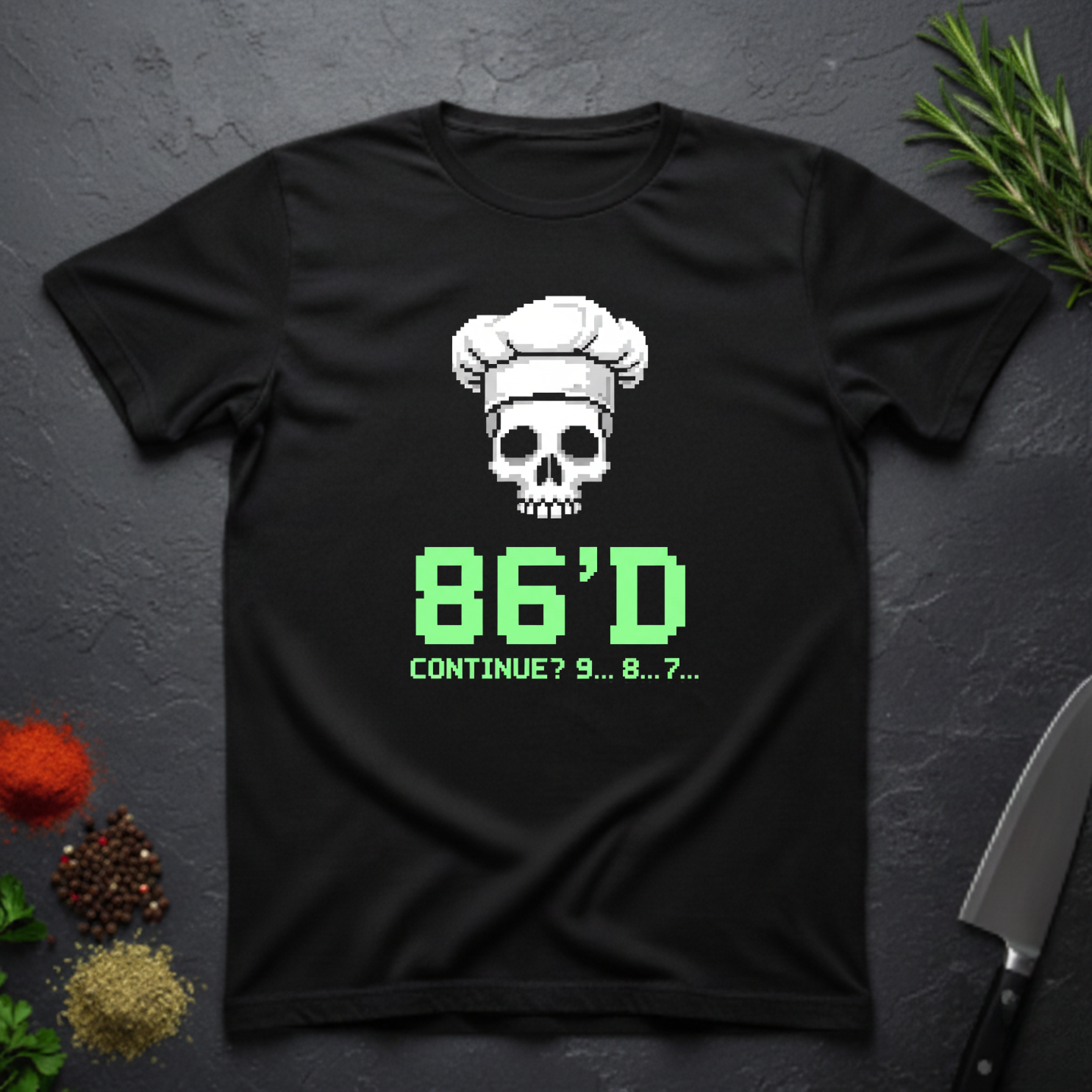 Black t-shirt with a skull wearing a chef's hat and text "86'd Continue? 9...8....7..." on a dark surface.