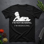 Black t-shirt with a graphic of a chef and text 'I'm not rushing. I'm reducing.' on a dark surface.