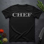 Black t-shirt with 'CHEF' printed in a decorative serif text on a dark surface with kitchen items.