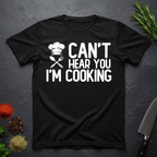Black t-shirt with 'Can't Hear You I'm Cooking' text on a dark surface with kitchen items.