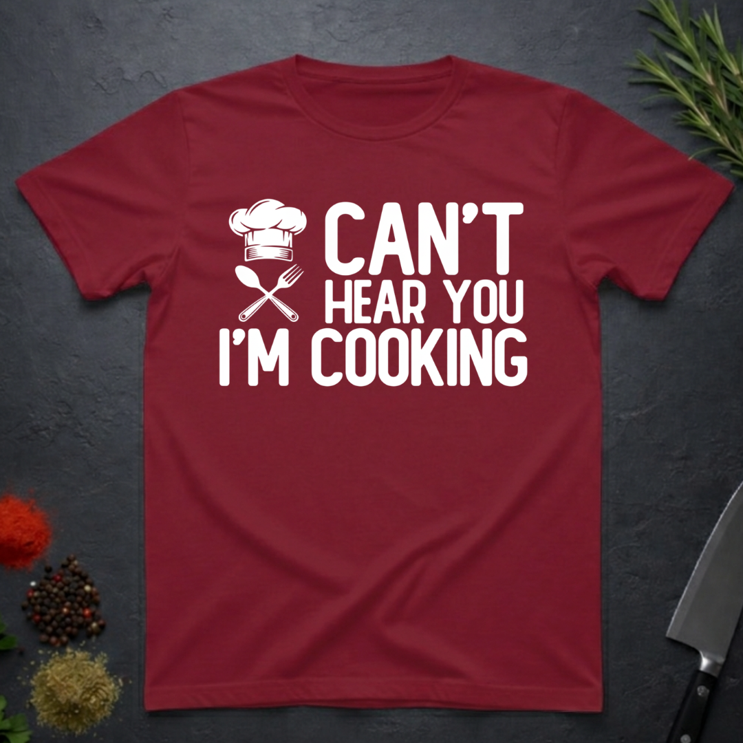 Cardinal Red t-shirt with 'Can't Hear You I'm Cooking' text on a dark surface with kitchen items.