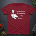 Cardinal red t-shirt with a male chef graphic and text "Your Opinion Wasn't Part of the Recipe" on a dark surface with kitchen items.