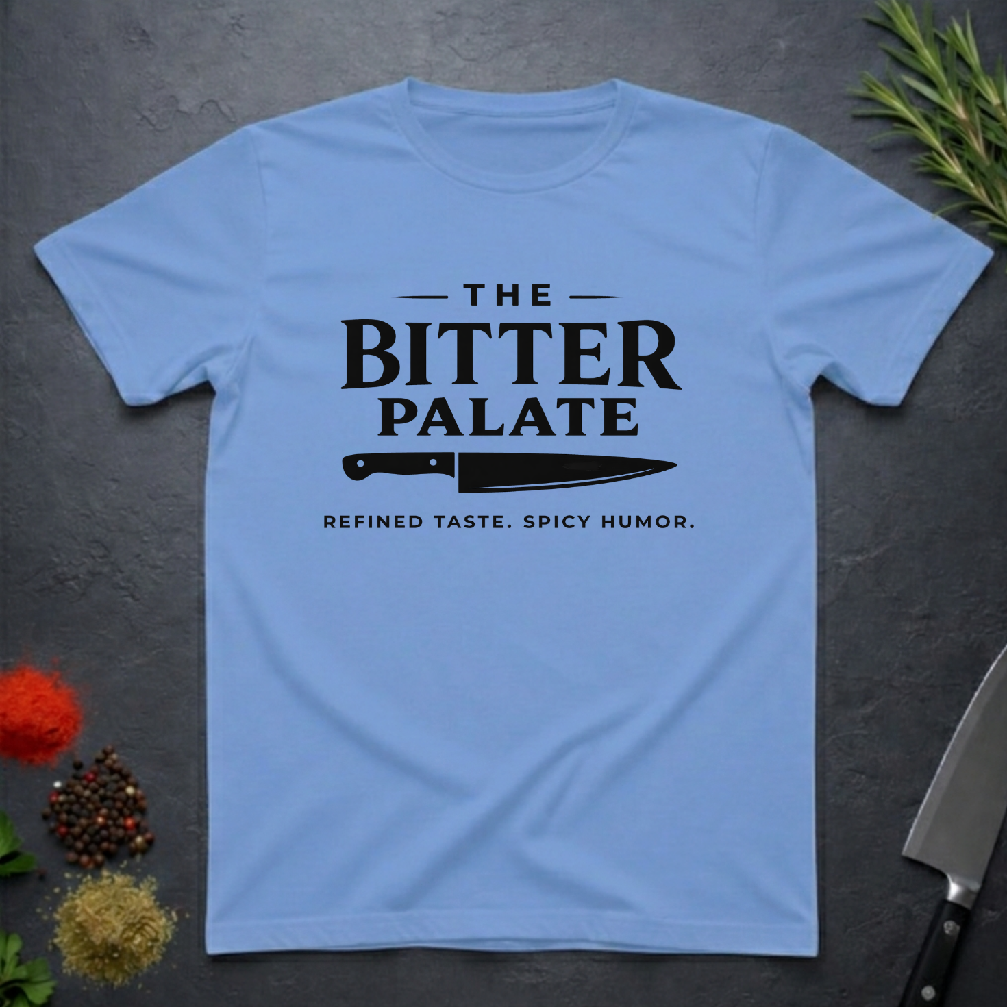 Carolina Blue t-shirt with 'The Bitter Palate' logo on a dark surface with kitchen items.