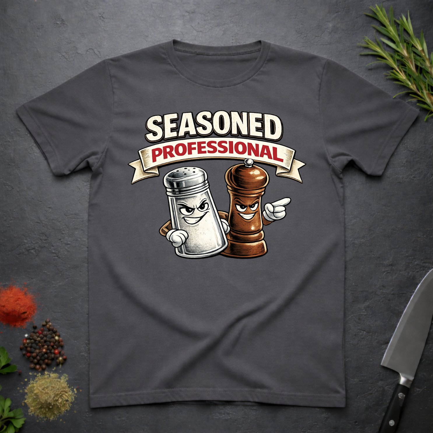 Charcoal Gray t-shirt with cartoon salt and pepper shakers and 'Seasoned Professional' text on a dark surface with spices and a knife.