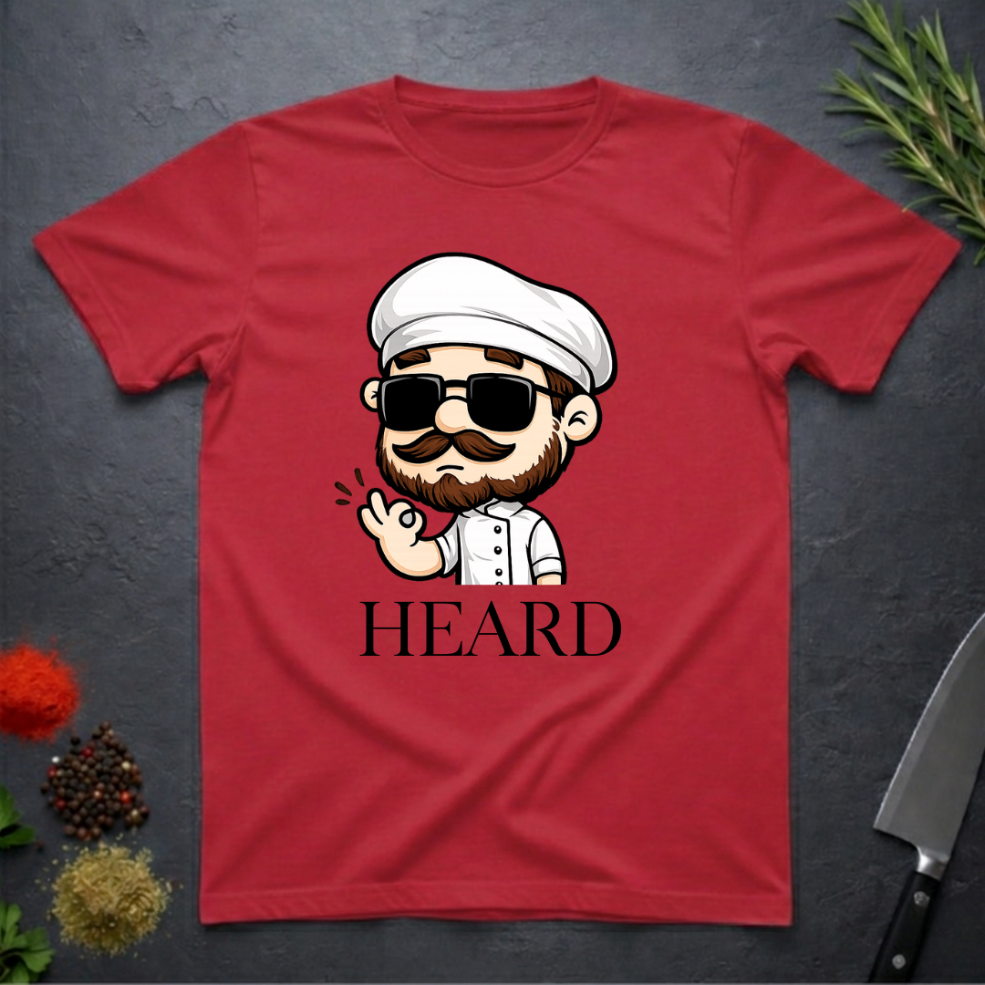 Cherry red t-shirt with a cartoon character chef and 'HEARD' text on a dark surface.
