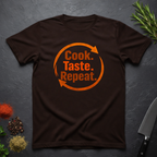 Chocolate brown t-shirt with bold text 'Cook. Taste. Repeat.' text inside of a large repeat symbol on a dark surface.