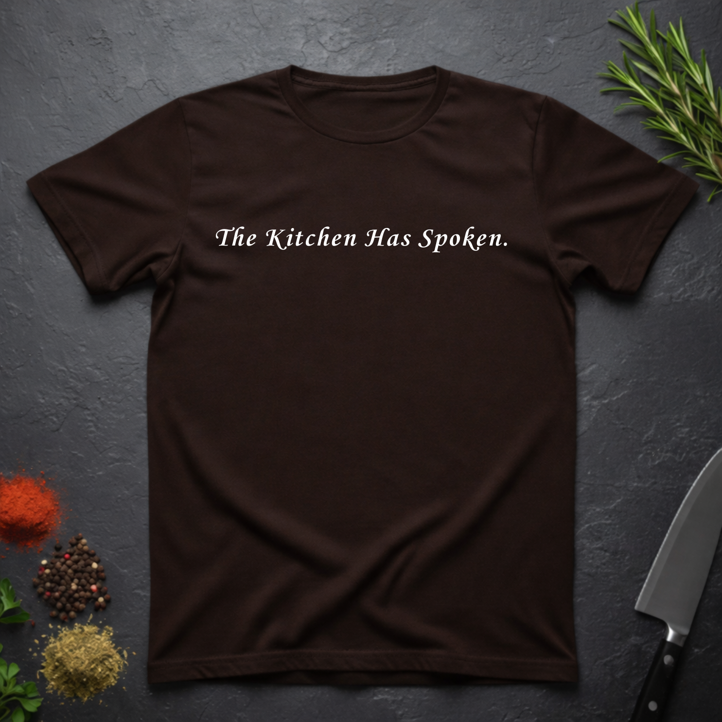 Chocolate Brown t-shirt with 'The Kitchen Has Spoken.' text on a dark surface with kitchen items.