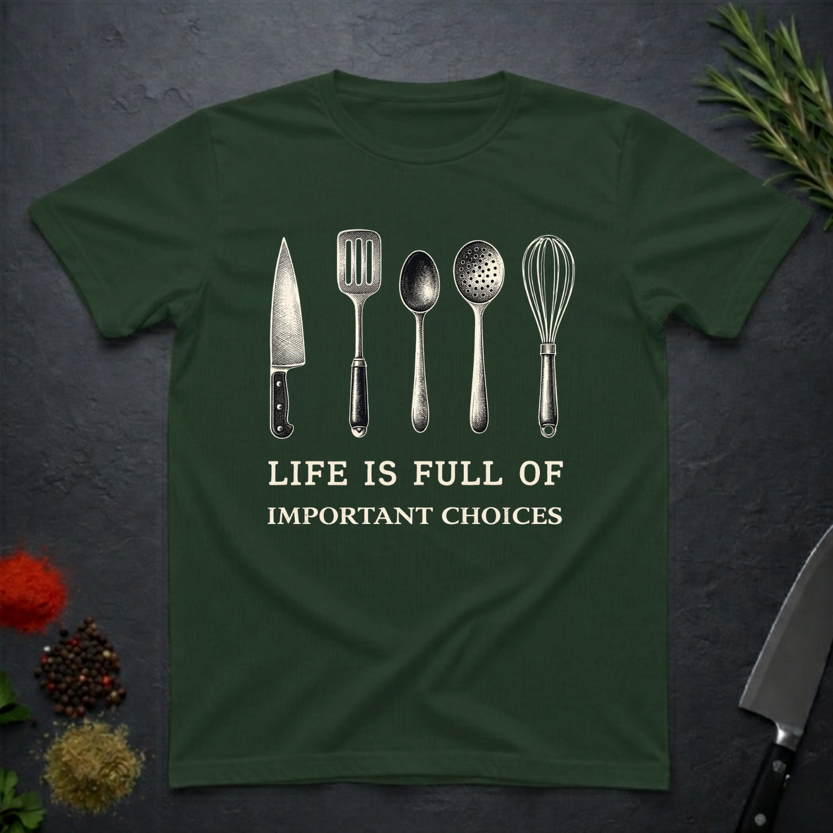 Forest green t-shirt with kitchen utensil graphics and text "Life is Full of Important Choices" on a dark surface.