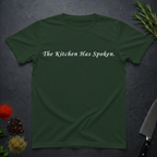 Forest Green t-shirt with 'The Kitchen Has Spoken.' text on a dark surface with kitchen items.