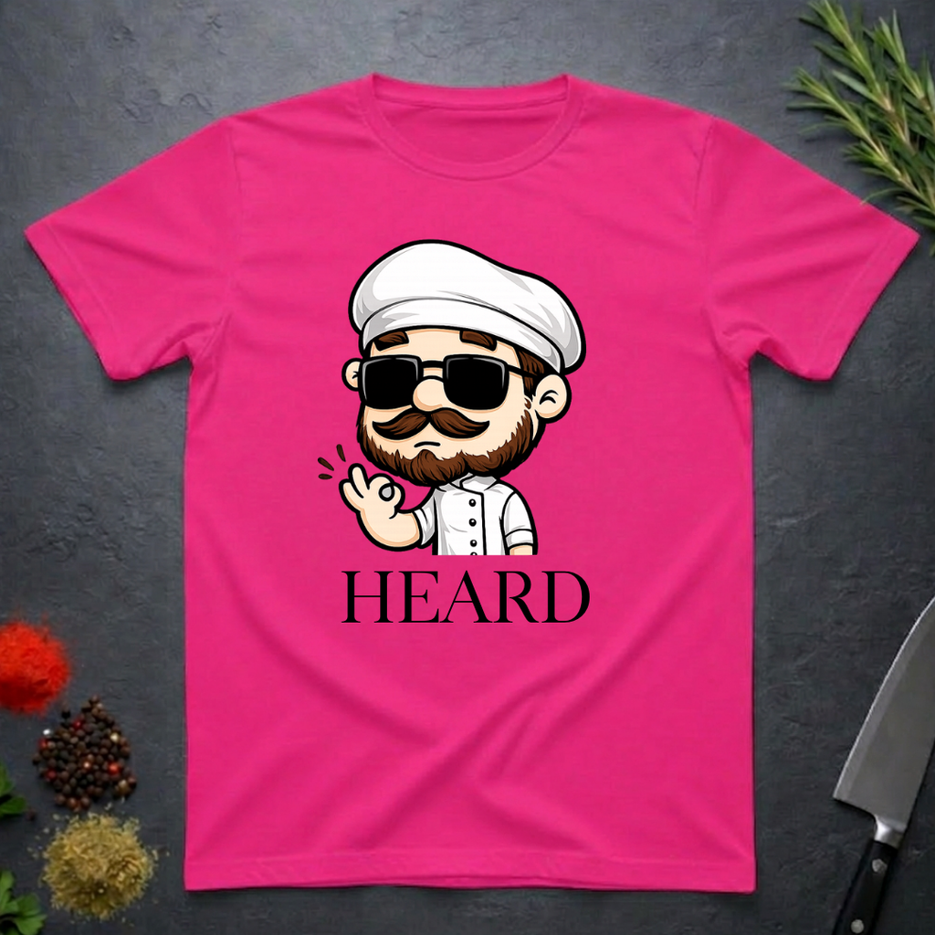 Heliconia pink t-shirt with a cartoon character chef and 'HEARD' text on a dark surface.