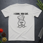 Ice Grey t-shirt with a graphic design and text 'I COOK. YOU EAT.' on a dark surface with kitchen items.