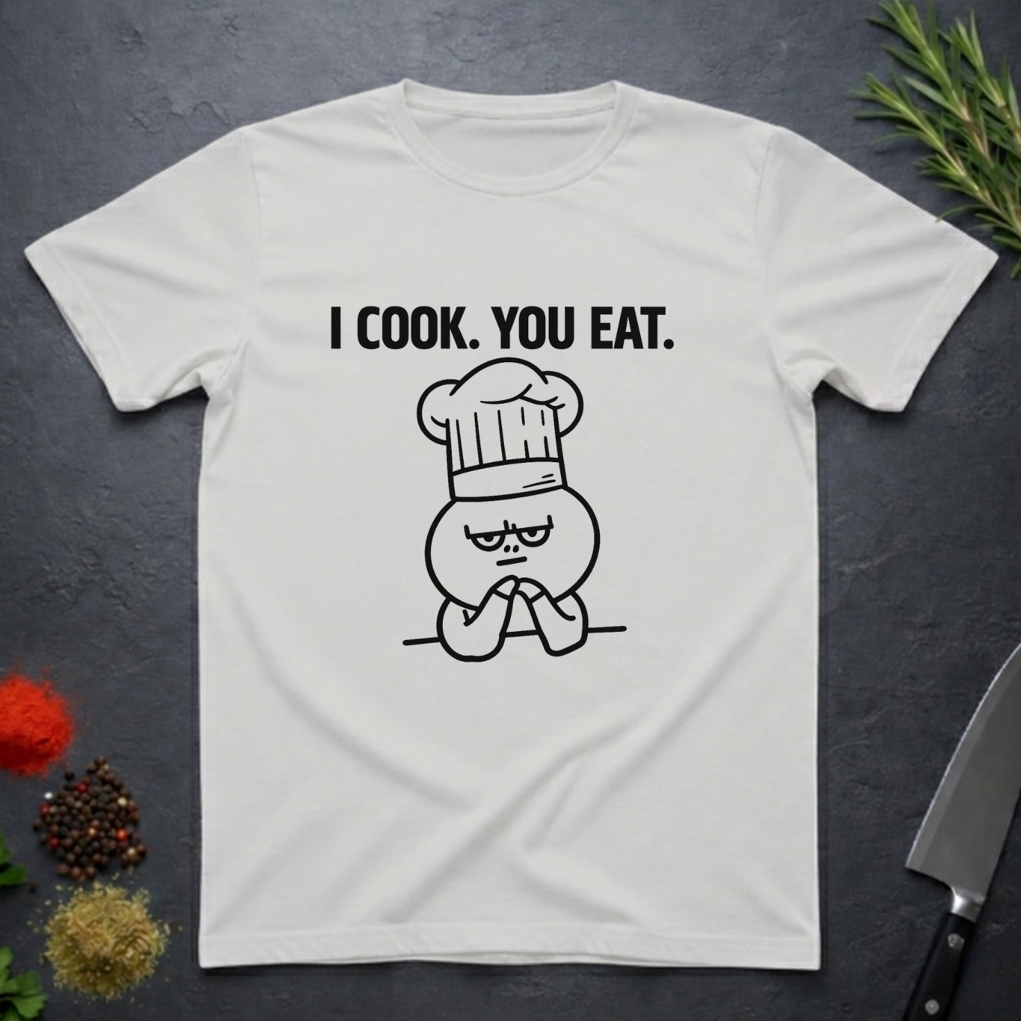 Ice Grey t-shirt with a graphic design and text 'I COOK. YOU EAT.' on a dark surface with kitchen items.