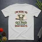 Ice grey t-shirt with skull and knife graphic and text "I'm Here to Get Paid the Play with Sharp objects" on a dark surface