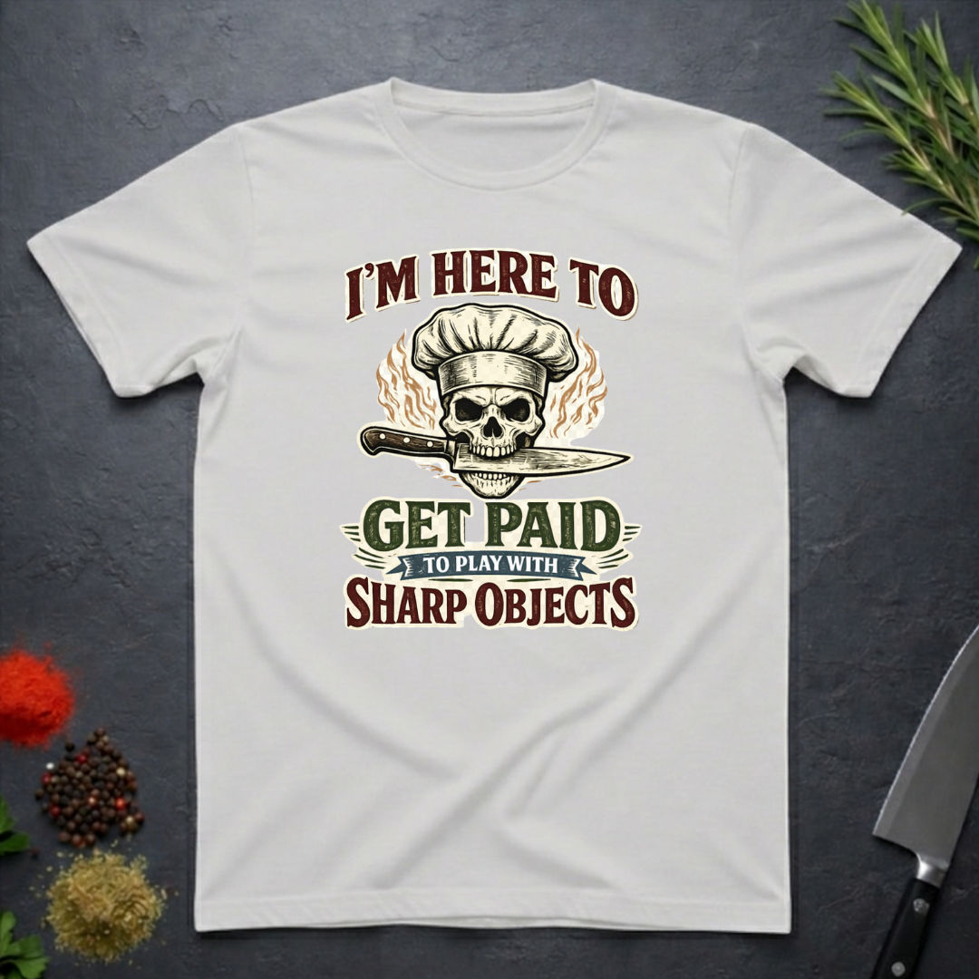 Ice grey t-shirt with skull and knife graphic and text "I'm Here to Get Paid the Play with Sharp objects" on a dark surface