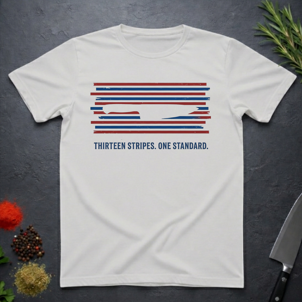 Ice grey t-shirt with 13 red, white, and blue stripes with a cut out (negative space) image of a chef's knife and text "THIRTEEN STRIPES. ONE STANDARD." on a dark surface.