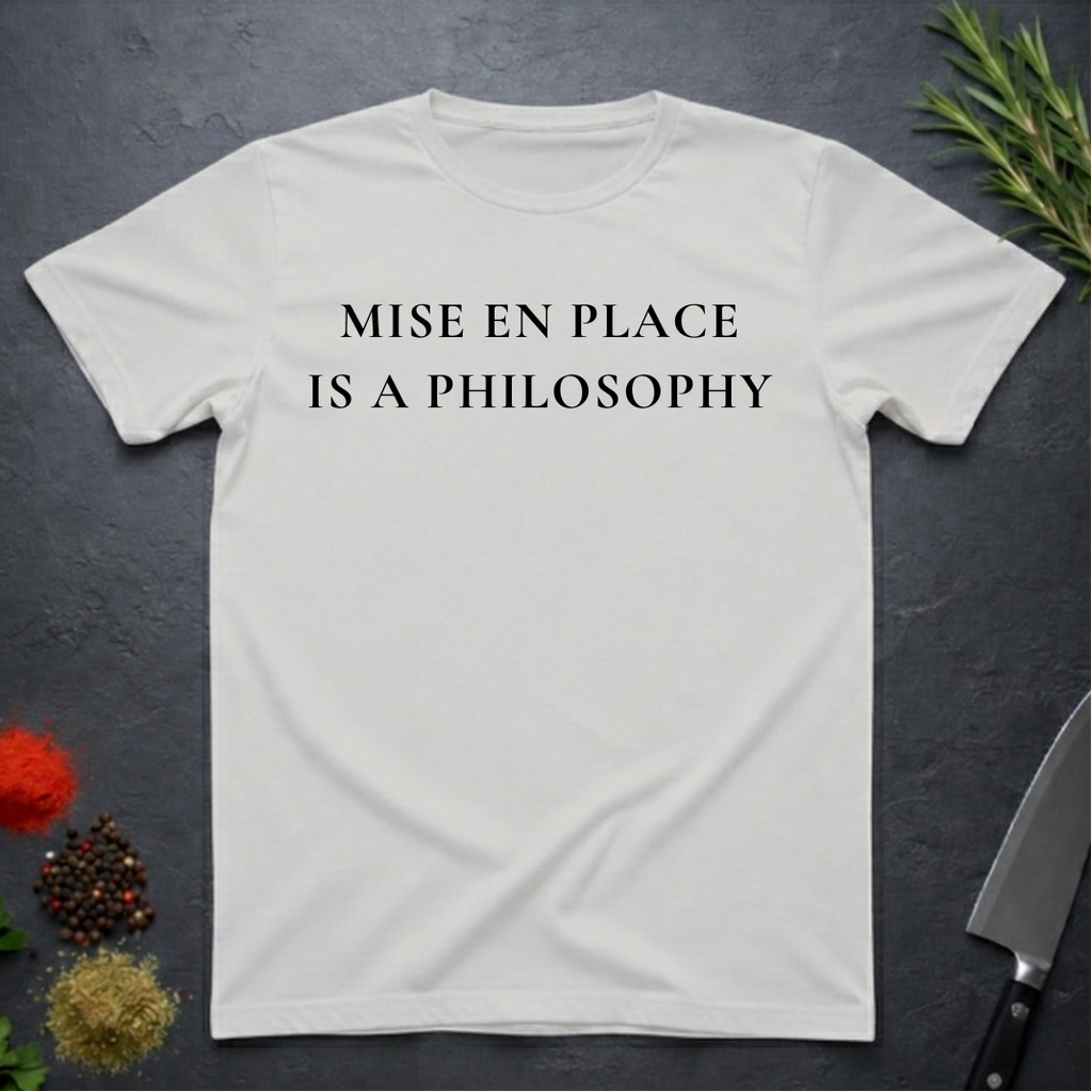 Ice Grey t-shirt with 'MISE EN PLACE IS A PHILOSOPHY' text on a dark surface with kitchen items.