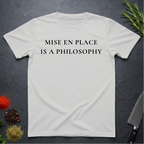 Ice Grey t-shirt with 'MISE EN PLACE IS A PHILOSOPHY' text on a dark surface with kitchen items.