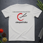 Ice grey t-shirt with Chopsticks graphic and text "I judge people by how they hold their chopsticks" on a dark surface with kitchen items.