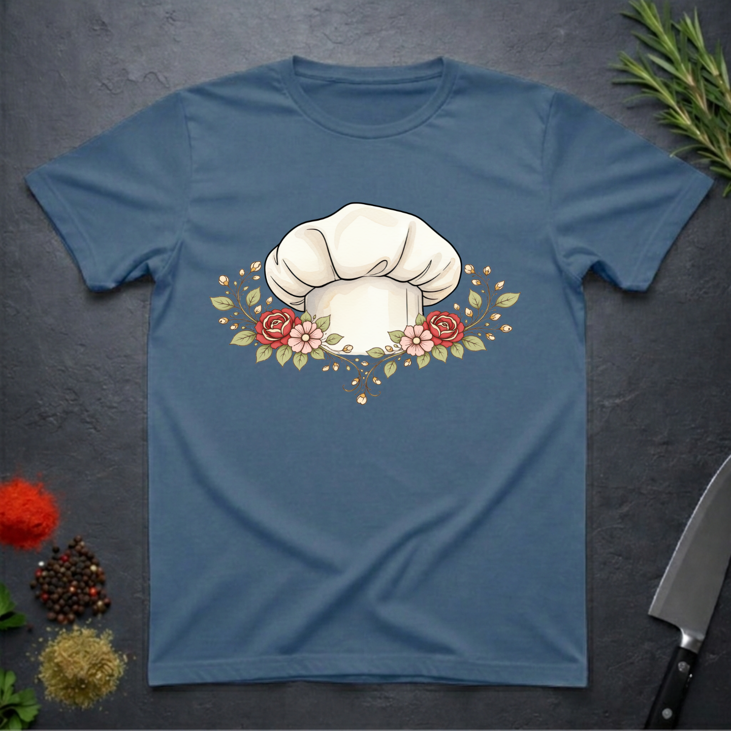 Indigo Blue t-shirt with a chef's hat and floral design on a dark surface.