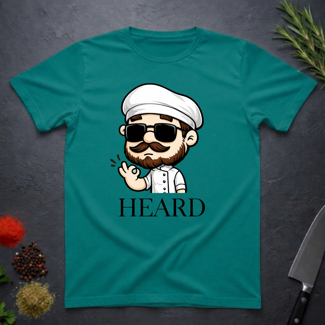Jade dome colored t-shirt with a cartoon character chef and 'HEARD' text on a dark surface.