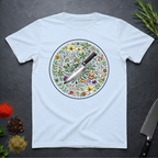 Light blue t-shirt with a circular knife and colored floral design on a dark surface.