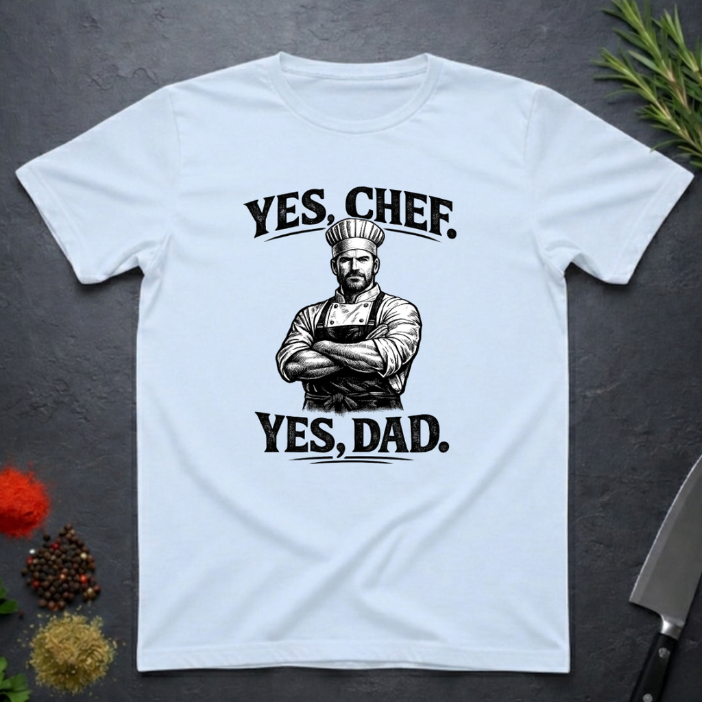 Light blue t-shirt with a graphic of a chef and text 'YES, CHEF. YES, DAD.' on a dark surface.