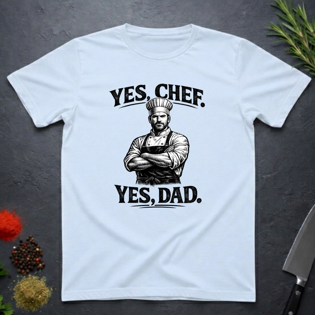 Light blue t-shirt with a graphic of a chef and text 'YES, CHEF. YES, DAD.' on a dark surface.