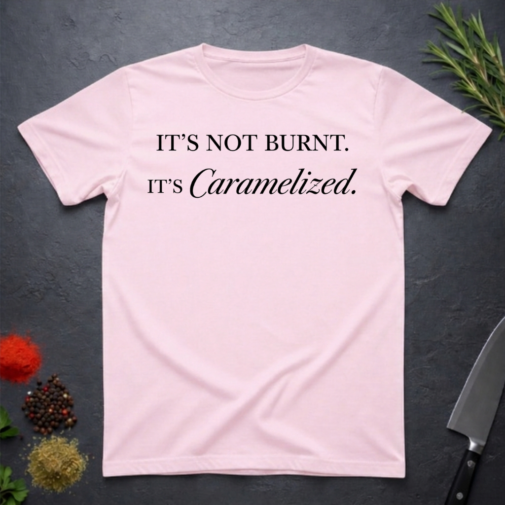 Light Pink t-shirt with text 'IT'S NOT BURNT. IT'S Caramelized.' on a dark surface with decorative elements.