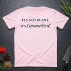 Light Pink t-shirt with text 'IT'S NOT BURNT. IT'S Caramelized.' on a dark surface with decorative elements.
